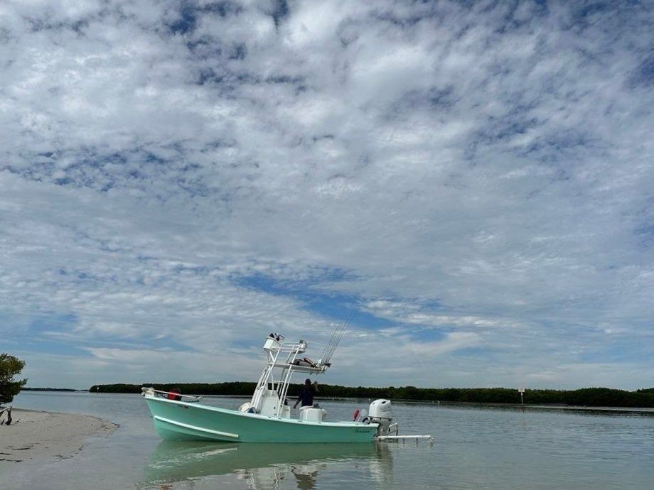 The Next Catch boat resting on a sandbar under a wide cloud filled sky