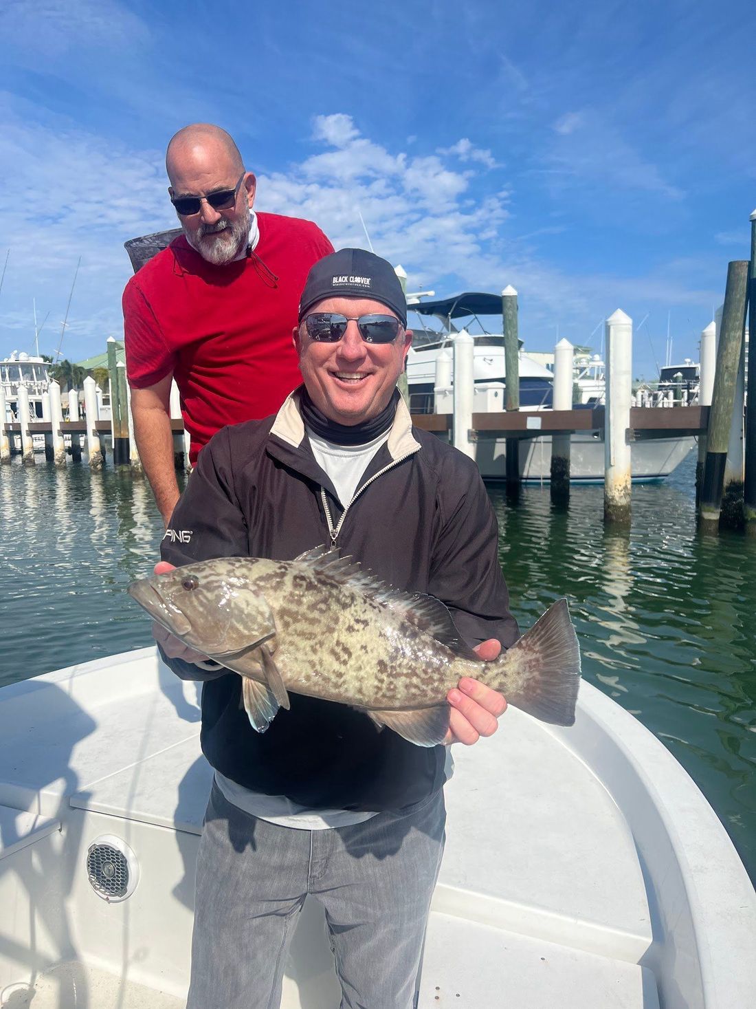 Two guests holding a gag grouper at the dock after a nearshore charter