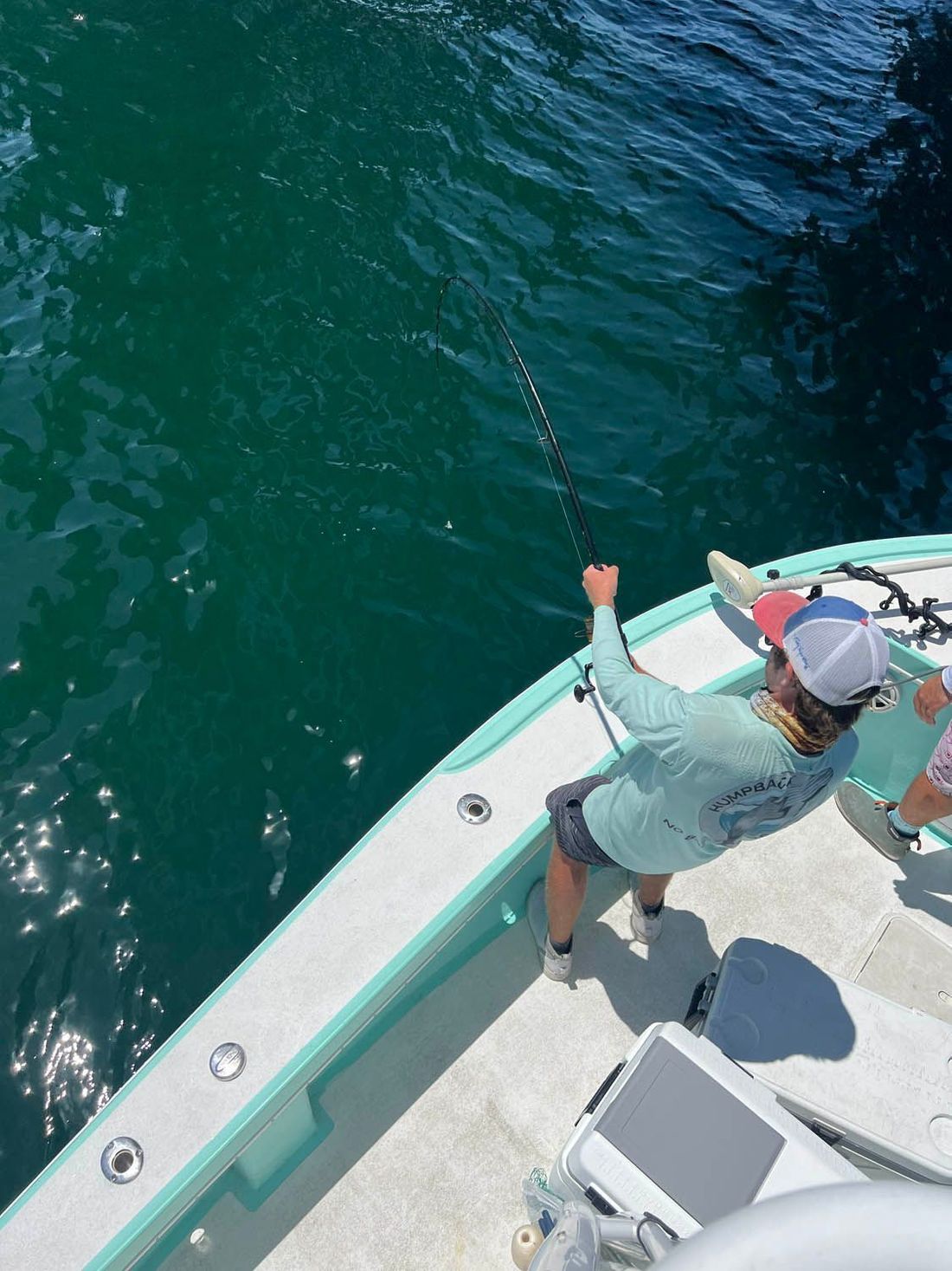 Angler hooked up and fighting a fish off the bow over green water