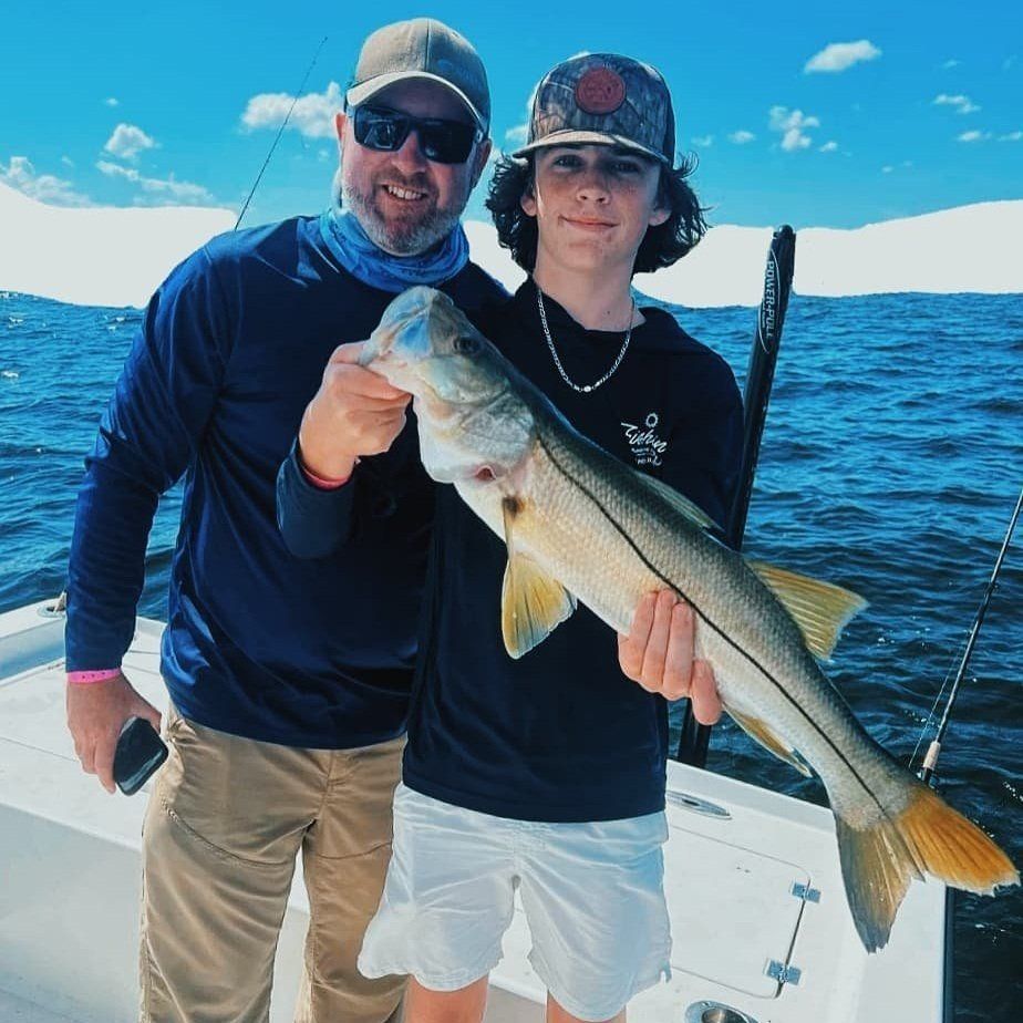 Father and son holding a long snook on the bow of the Next Catch boat