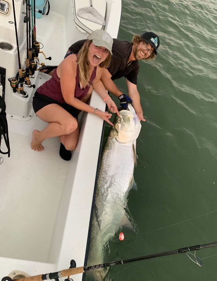 Two guests laughing beside a tarpon held at the gunwale