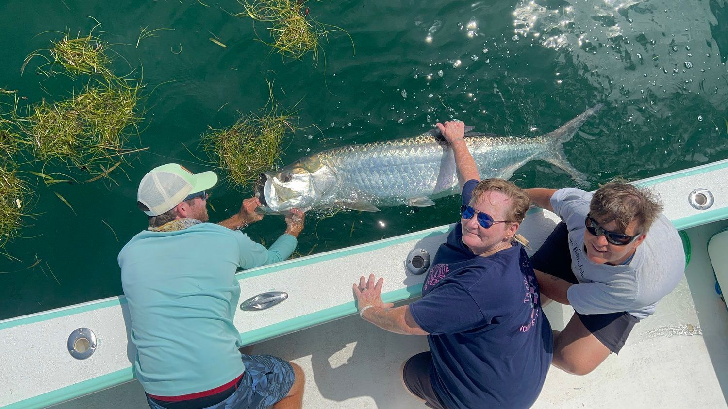 Captain Bryan holding a tarpon at the rail while two guests watch from the deck